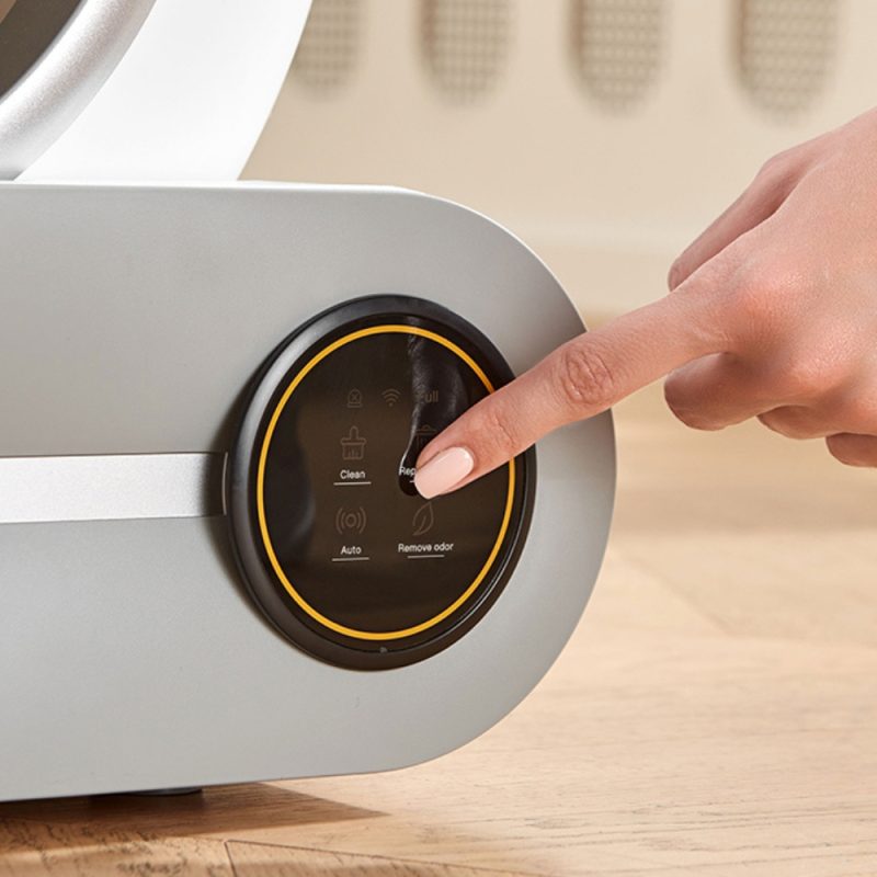 Hand pressing control panel on automatic self-cleaning cat litter box with touchscreen display showing Clean, Auto, and Remove odor functions